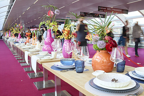Ein Foto von einer Reihe Tischen mit ausgestelltem Geschirr, darunter Blumenwasen, Teller, Weingläser und mehr. 