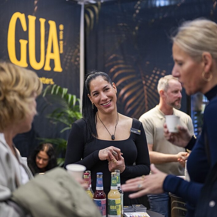 Messestand mit Getränken und Gesprächssituation vor einem GUA-Branding-Hintergrund.
