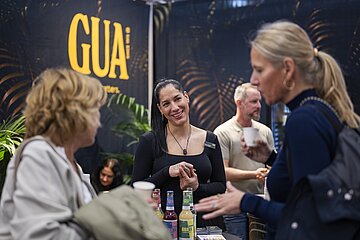 Messestand mit Getränken und Gesprächssituation vor einem GUA-Branding-Hintergrund.