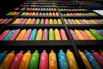 Regale voller bunter Flaschen, in mehreren Reihen angeordnet. Die Flaschen sind in kräftigen Farben wie Pink, Gelb, Grün, Blau und Orange gestaltet und tragen auffällige Schriftzüge.