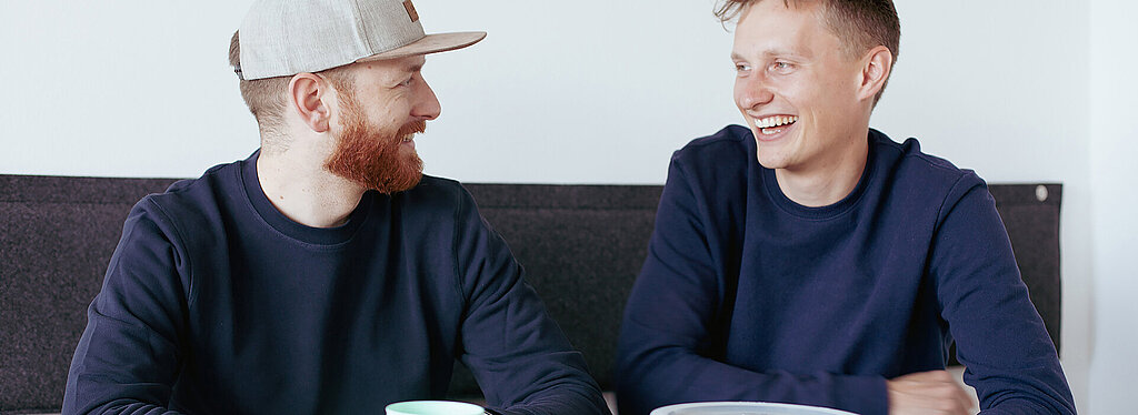 RECUP Gründer Eckert & Pachaly sitzen lachend an einem Tisch, im Vordergrund verschiedene Dosen von RECUP