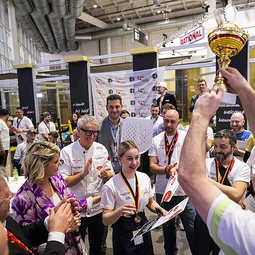 Teilnehmende der Pizza Experience und ein Mann sind zu sehen, welcher einen Pokal hochhält