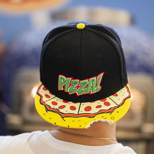 Eine Aufnahme eines Kopfes von hinten, auf welcher eine Kappe mit der Aufrschrift "Pizza" aufgesetzt ist, wobei die Kappe in die andere Richtung gedreht ist.