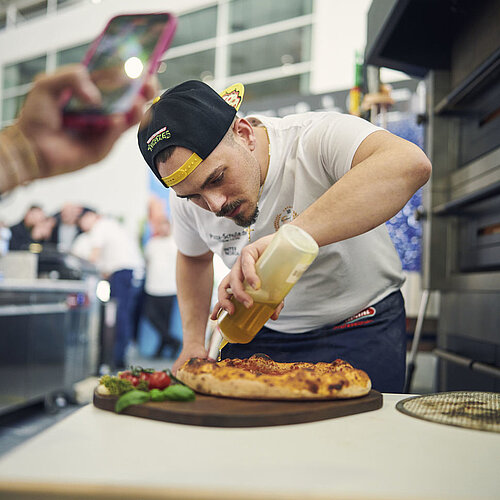 Pizzabäcker beträufelt eine Pizza mit Olivenöl. 